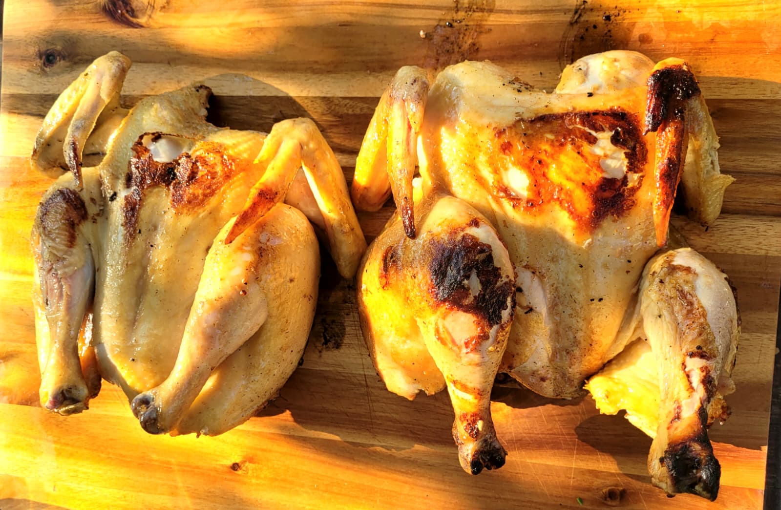 Two golden roast chickens on a wooden board