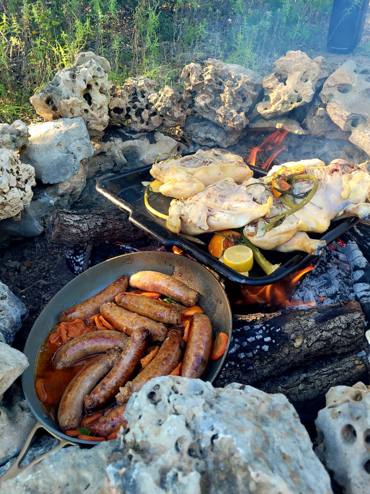 Sausages and chickens cooking over an open fire in a stone firepit